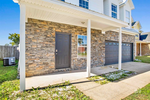 doorway to property with covered porch, cooling unit, and a garage