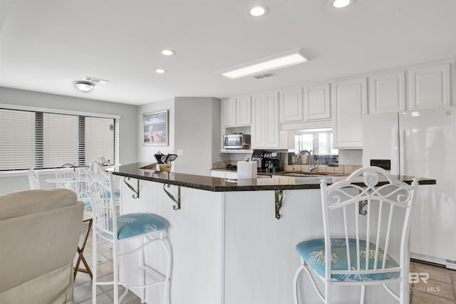 kitchen with a sink, white cabinetry, white fridge with ice dispenser, stainless steel microwave, and a kitchen bar