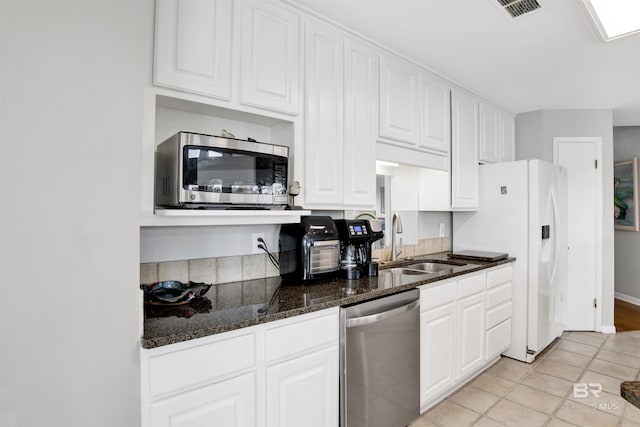 kitchen featuring dark stone countertops, appliances with stainless steel finishes, white cabinets, and a sink