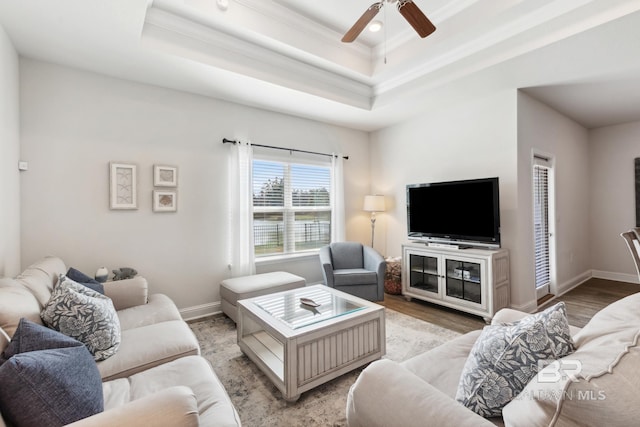 living room with a raised ceiling, crown molding, light hardwood / wood-style flooring, and ceiling fan