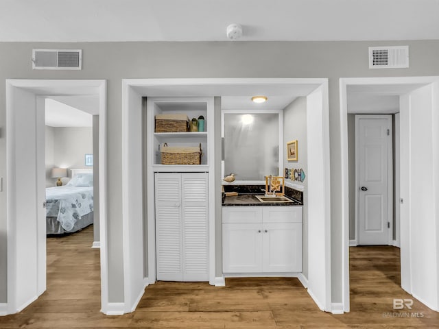 bar featuring white cabinets, light wood-type flooring, dark stone counters, and sink