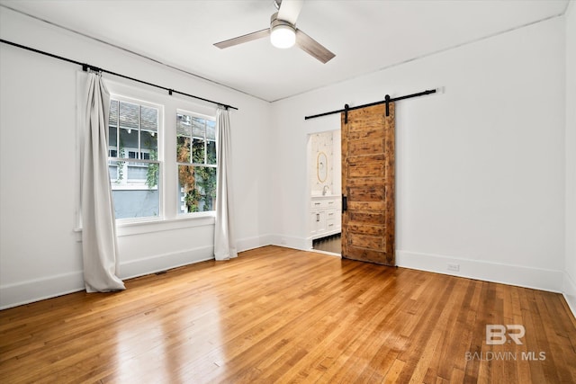 spare room featuring a barn door, ceiling fan, and light hardwood / wood-style flooring