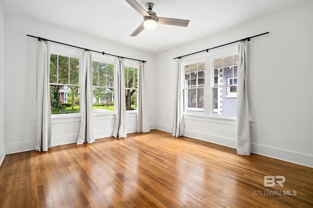 empty room with a healthy amount of sunlight, ceiling fan, and light hardwood / wood-style floors