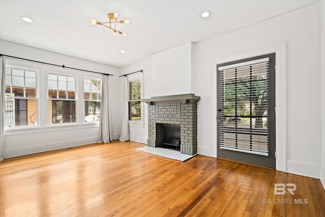 unfurnished living room with light hardwood / wood-style flooring, a notable chandelier, and a brick fireplace