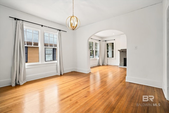 spare room featuring plenty of natural light, light hardwood / wood-style flooring, and a brick fireplace