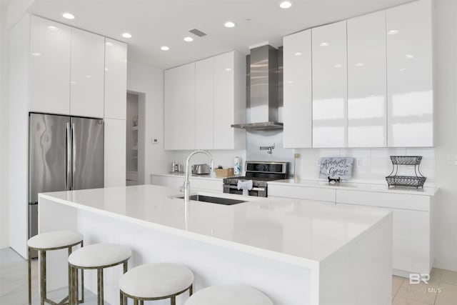 kitchen with stainless steel appliances, a breakfast bar area, wall chimney range hood, and white cabinets