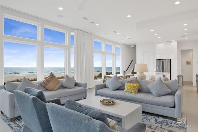 living room featuring a water view, a wealth of natural light, light tile patterned floors, and a view of the beach