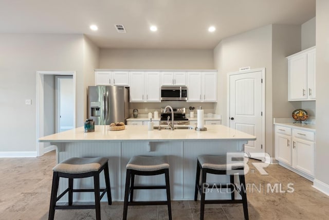 kitchen featuring appliances with stainless steel finishes, a kitchen island with sink, light countertops, and white cabinets