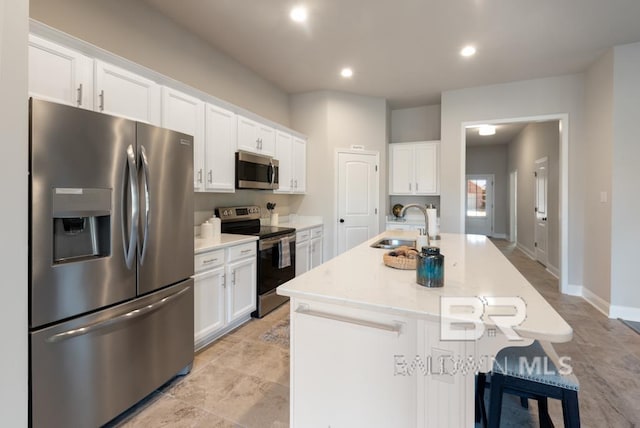 kitchen with stainless steel appliances, white cabinets, light countertops, and an island with sink