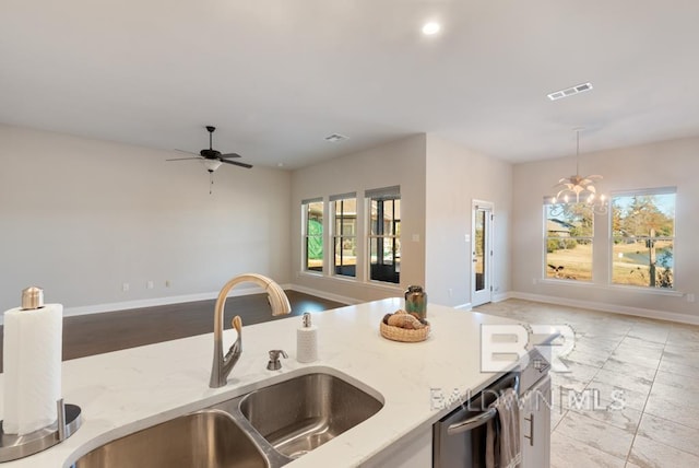 kitchen with sink, ceiling fan with notable chandelier, light stone countertops, and hanging light fixtures