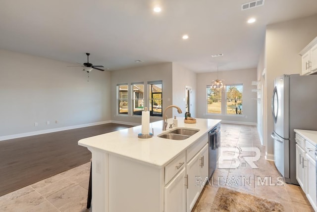 kitchen with stainless steel appliances, light countertops, open floor plan, a sink, and an island with sink