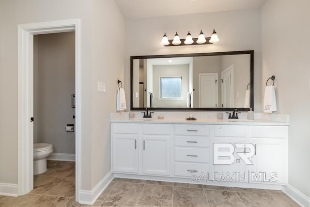 bathroom with baseboards, a sink, toilet, and double vanity