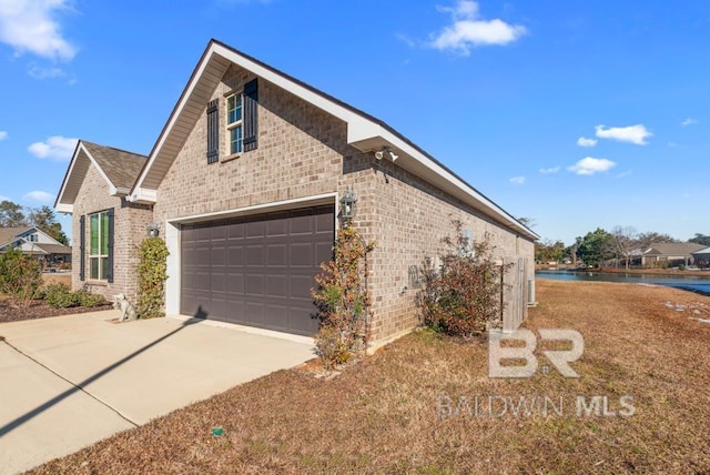 view of side of home featuring a garage, driveway, brick siding, and a water view