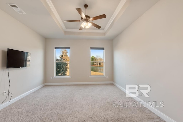 spare room featuring light colored carpet, a ceiling fan, visible vents, baseboards, and a raised ceiling