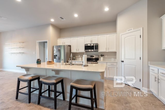 kitchen with white cabinetry, stainless steel appliances, a breakfast bar, and an island with sink