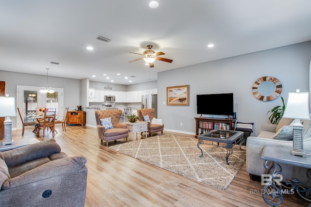 living room featuring light hardwood / wood-style flooring and ceiling fan with notable chandelier