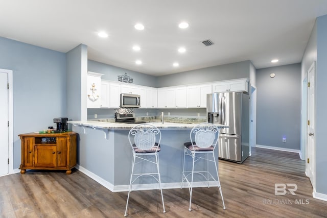 kitchen featuring white cabinets, a kitchen breakfast bar, dark hardwood / wood-style flooring, kitchen peninsula, and stainless steel appliances