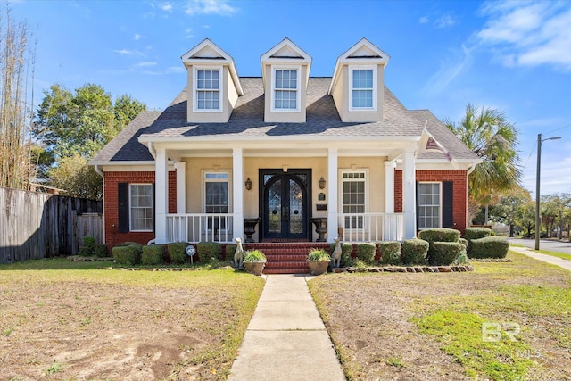 view of front facade with fence, french doors, covered porch, a shingled roof, and brick siding