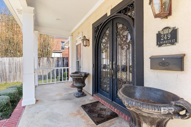 entrance to property with stucco siding, a porch, and fence