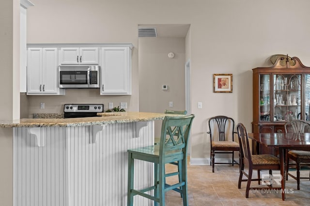 14766 Sonoma Blvd, Silverhill, AL 36576 - kitchen with light stone counters, a breakfast bar, appliances with stainless steel finishes, visible vents, and white cabinets