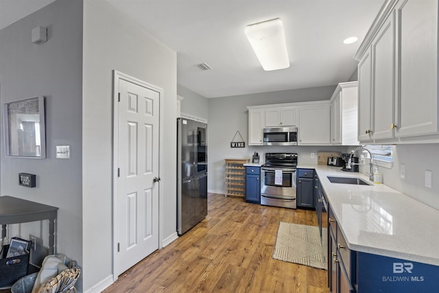 kitchen featuring sink, blue cabinetry, stainless steel appliances, light hardwood / wood-style floors, and white cabinets