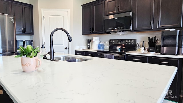 kitchen with appliances with stainless steel finishes, light stone countertops, a kitchen island with sink, and sink