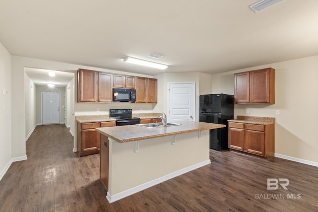 kitchen with sink, dark wood-type flooring, a kitchen island with sink, a breakfast bar, and black appliances