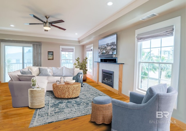 living area featuring a glass covered fireplace, visible vents, crown molding, and wood finished floors