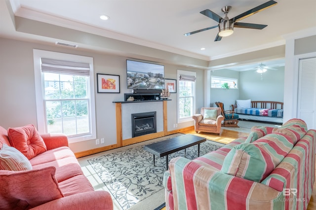 living area featuring baseboards, a glass covered fireplace, ornamental molding, a tray ceiling, and recessed lighting