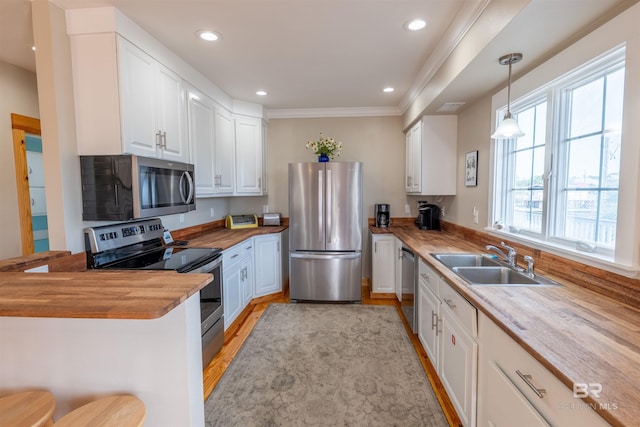 kitchen with white cabinets, butcher block countertops, appliances with stainless steel finishes, hanging light fixtures, and a sink