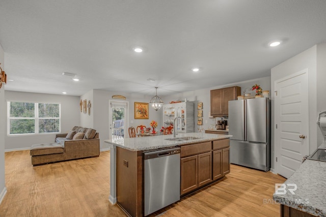 kitchen with appliances with stainless steel finishes, an island with sink, sink, hanging light fixtures, and light hardwood / wood-style flooring