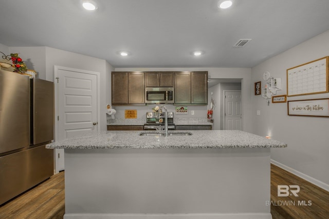 kitchen with sink, light stone counters, a kitchen island with sink, and stainless steel appliances