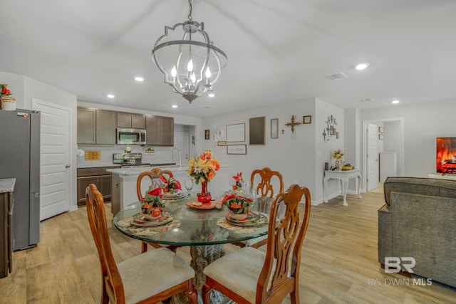 dining space with sink, light wood-type flooring, and an inviting chandelier