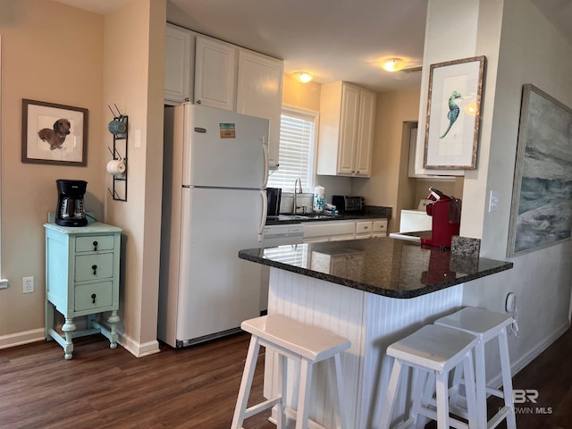 kitchen with white fridge, dark hardwood / wood-style floors, a kitchen breakfast bar, kitchen peninsula, and white cabinetry