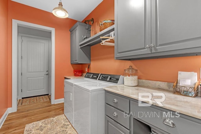 clothes washing area with washing machine and dryer, cabinets, and light hardwood / wood-style flooring