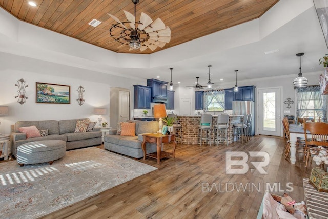 living room with wooden ceiling, ornamental molding, dark hardwood / wood-style floors, ceiling fan, and a tray ceiling