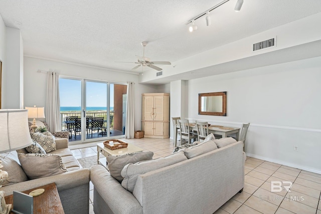 tiled living room featuring track lighting, a water view, ceiling fan, and a textured ceiling