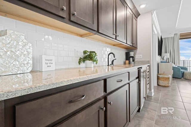 kitchen featuring backsplash, sink, light tile patterned flooring, light stone counters, and dark brown cabinetry