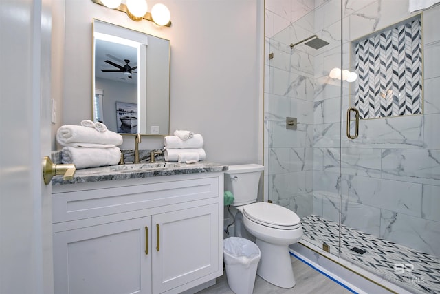 bathroom with a shower with shower door, hardwood / wood-style flooring, vanity, ceiling fan, and toilet