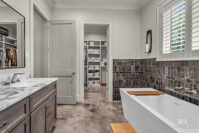 bathroom featuring a soaking tub, vanity, a walk in closet, concrete flooring, and tile walls