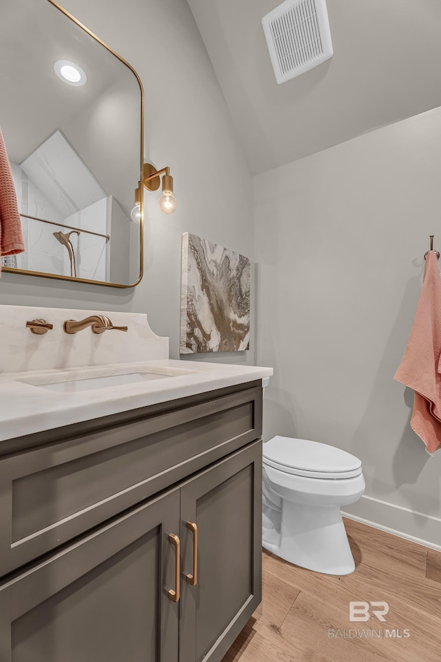 bathroom with lofted ceiling, wood finished floors, toilet, vanity, and baseboards