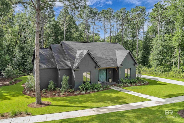 view of front of house with a front yard, roof with shingles, and view of wooded area