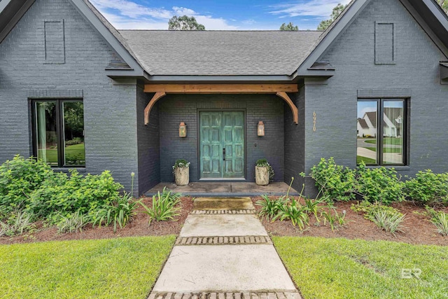 entrance to property with brick siding, roof with shingles, and a lawn