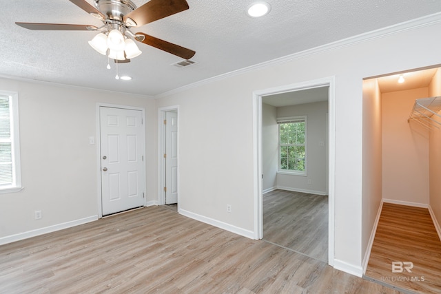 unfurnished bedroom featuring ceiling fan, light hardwood / wood-style flooring, a textured ceiling, a walk in closet, and ornamental molding