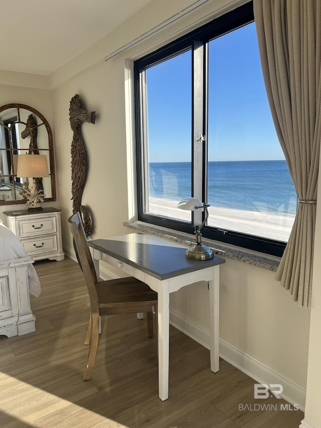 unfurnished dining area with a water view, a beach view, and wood-type flooring