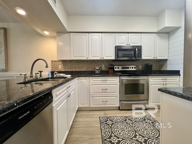 kitchen featuring sink, appliances with stainless steel finishes, white cabinetry, dark stone countertops, and tasteful backsplash