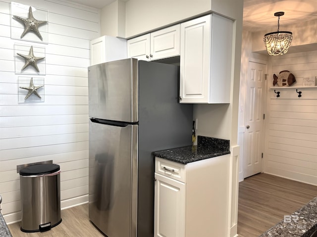 kitchen with pendant lighting, wooden walls, white cabinetry, stainless steel fridge, and light wood-type flooring