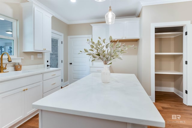 kitchen featuring a sink, a kitchen island, white cabinets, and ornamental molding