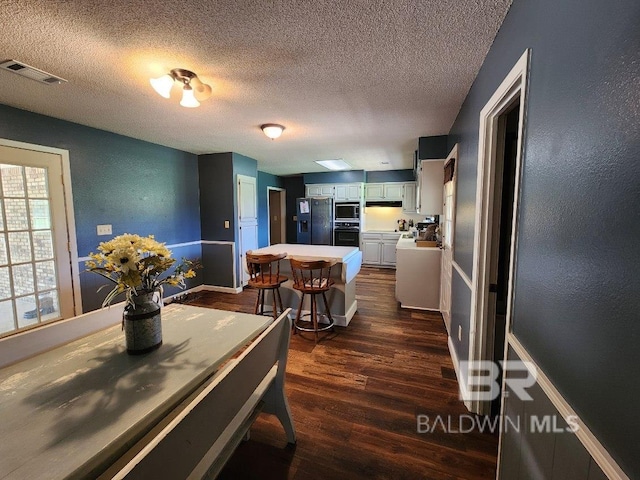 dining space featuring baseboards, visible vents, dark wood finished floors, a textured wall, and a textured ceiling