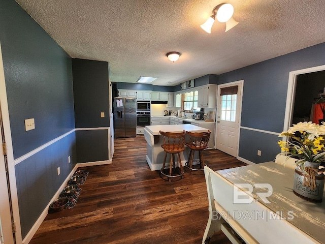 kitchen featuring oven, light countertops, fridge with ice dispenser, stainless steel microwave, and dark wood finished floors